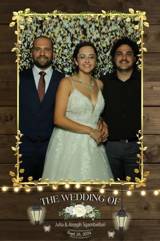 Bride with two guests at a Hamilton wedding photo booth with a greenery and lights backdrop