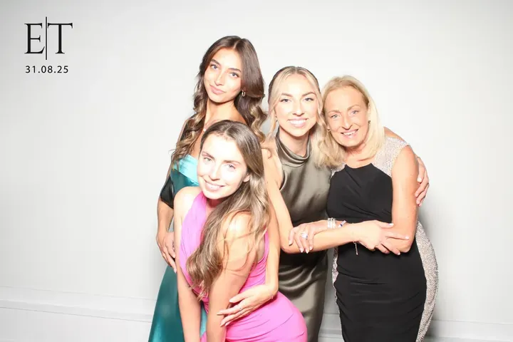 Four wedding guests hugging at the photo booth on a white backdrop
