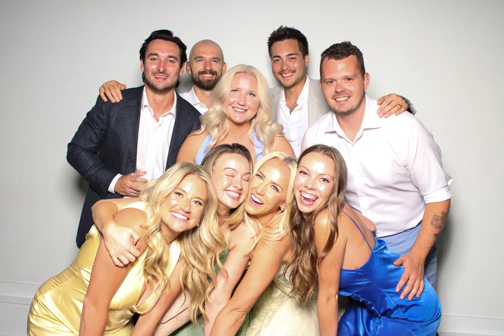 Big group of wedding guests crowded into the photo booth on a white wall